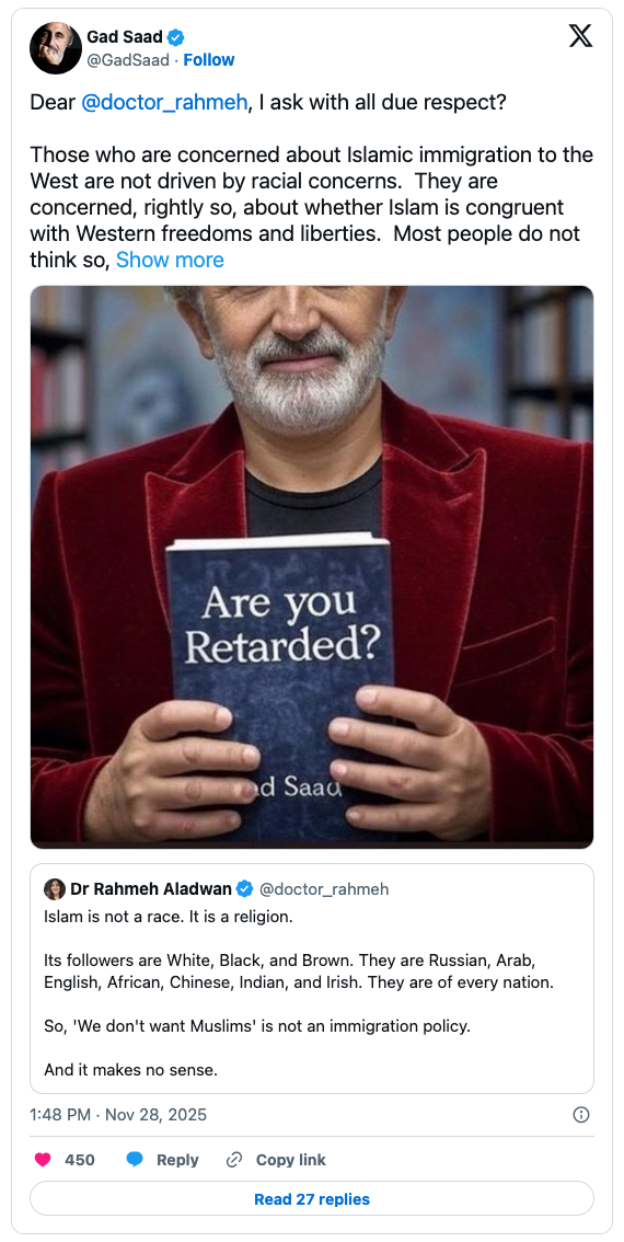 A man with a gray beard and mustache wearing a red blazer holds a book titled 'Are you Retarded?' by Gad Saad. The background is slightly blurred, focusing on the man and the book.