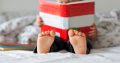 Sweet toddler boy, reading book at home, sitting in bed, lots of books around him